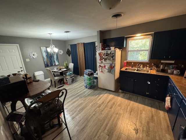 kitchen with freestanding refrigerator, light wood-style flooring, dark cabinetry, a sink, and decorative light fixtures