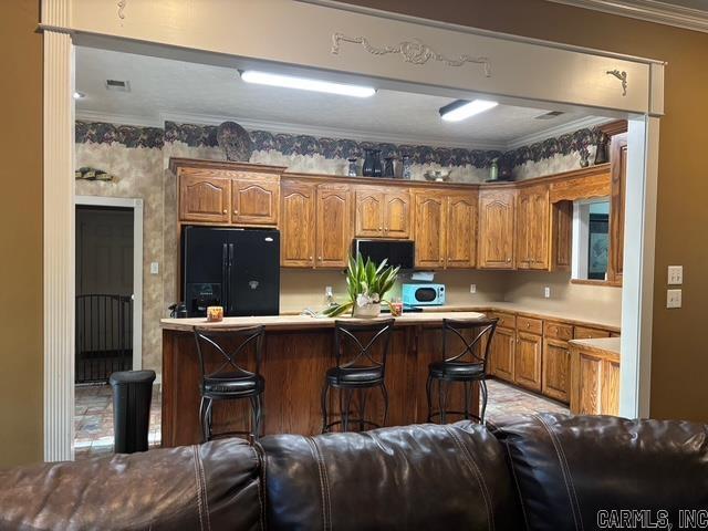 115 Las Colinas St, Conway, AR 72034 - kitchen featuring black fridge, a kitchen bar, brown cabinetry, crown molding, and light countertops