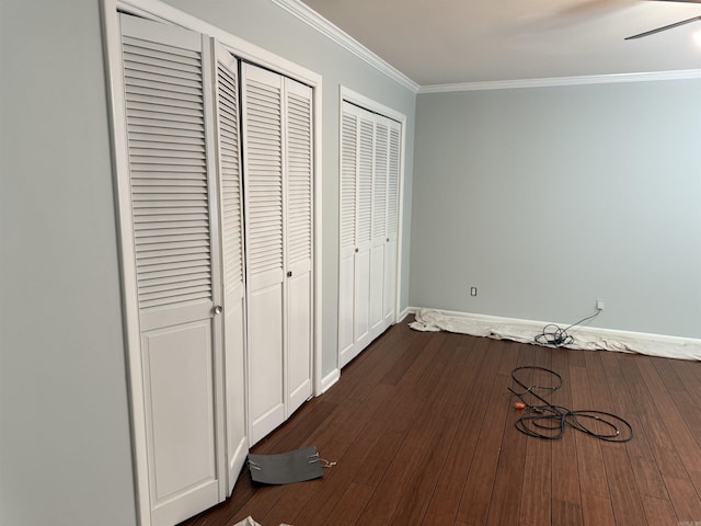 unfurnished bedroom featuring two closets, ornamental molding, dark wood-style flooring, and baseboards