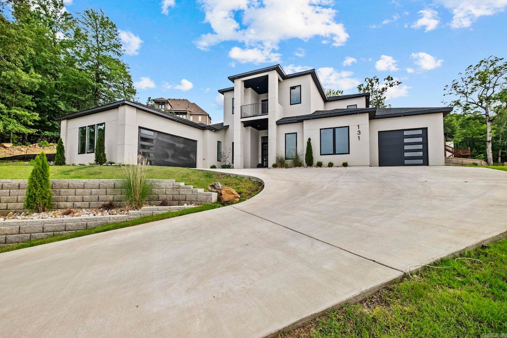 modern home with curved driveway, stucco siding, a balcony, and an attached garage