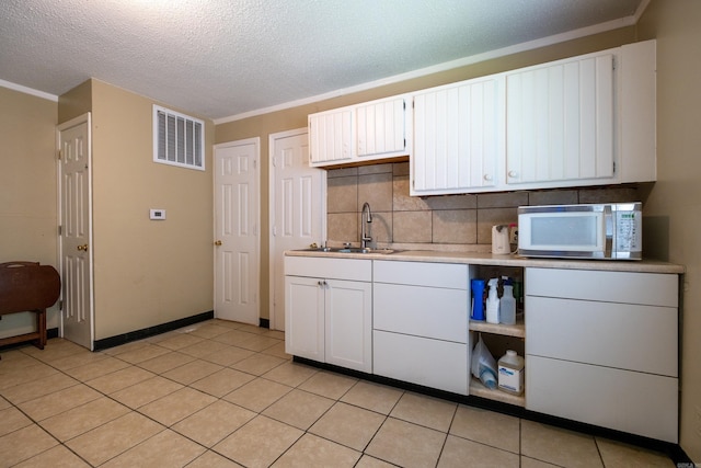 1411 Maple St, North Little Rock, AR 72114 - kitchen featuring white microwave, a sink, light countertops, tasteful backsplash, and white cabinetry