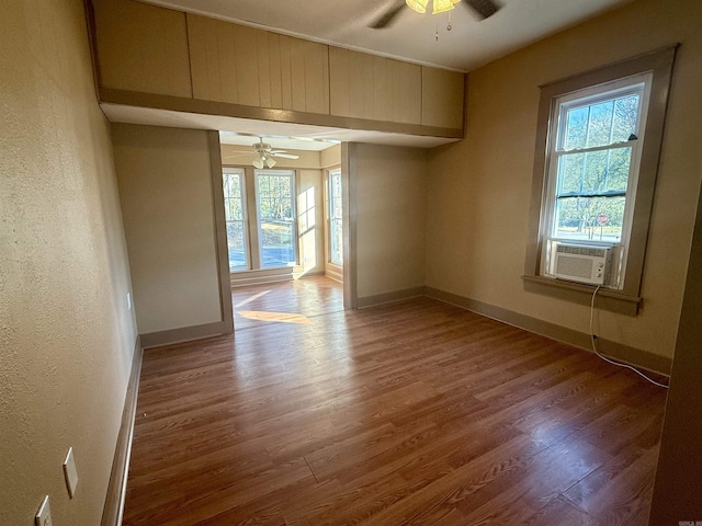 unfurnished room featuring a ceiling fan, wood finished floors, cooling unit, baseboards, and a textured wall