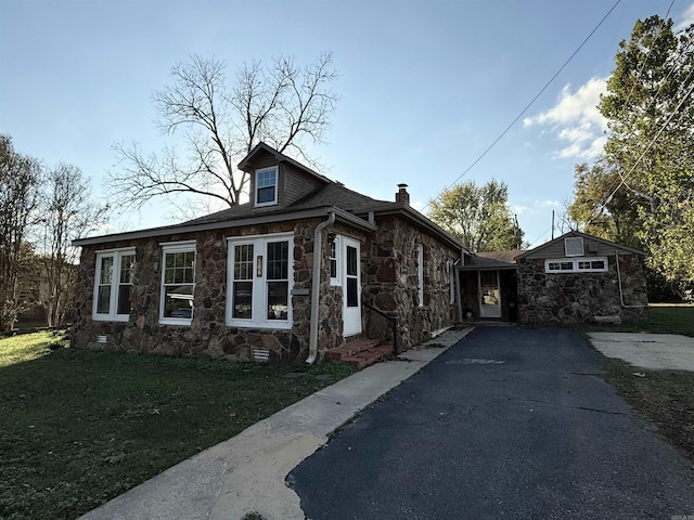 view of front facade with stone siding, a chimney, a front yard, and entry steps
