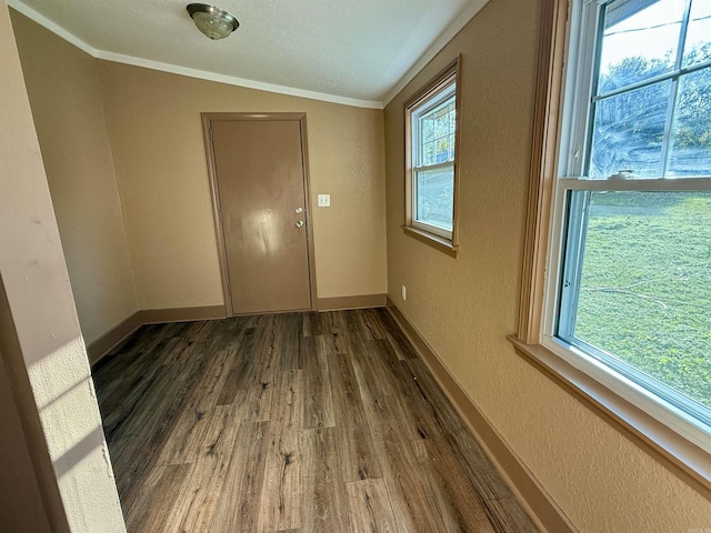 empty room featuring a textured wall, dark wood-type flooring, crown molding, and baseboards
