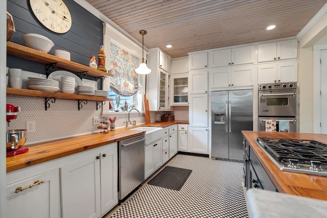 kitchen featuring butcher block countertops, appliances with stainless steel finishes, a sink, white cabinets, and decorative backsplash