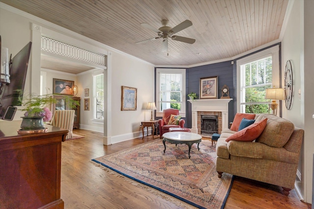 living room featuring healthy amount of natural light, ornamental molding, a ceiling fan, a brick fireplace, and wood finished floors