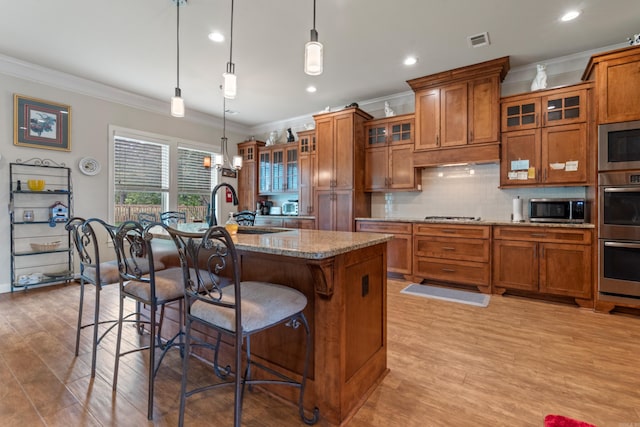 kitchen with brown cabinets, ornamental molding, appliances with stainless steel finishes, a kitchen bar, and recessed lighting