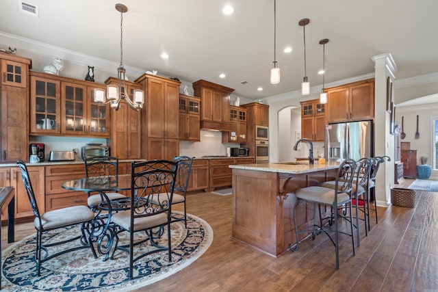 kitchen with brown cabinets, stainless steel appliances, a sink, arched walkways, and crown molding
