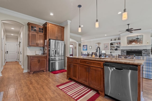 kitchen with stainless steel appliances, arched walkways, ornamental molding, brown cabinets, and ceiling fan