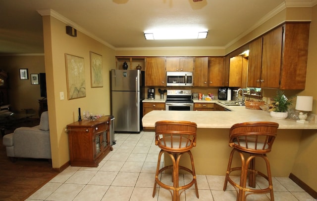 2102 N 22nd St, Paragould, AR 72450 - kitchen featuring appliances with stainless steel finishes, light countertops, brown cabinets, a peninsula, and crown molding