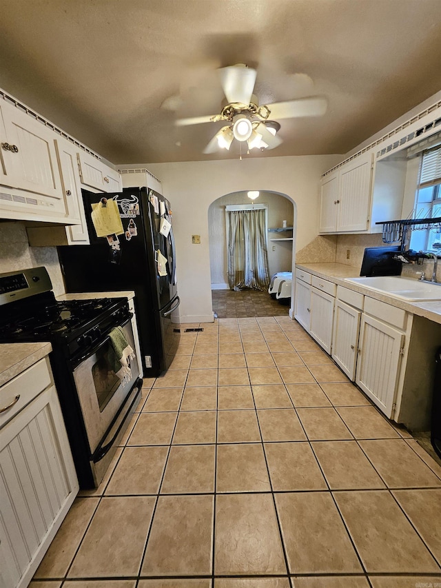 1421 W 25th St, North Little Rock, AR 72114 - kitchen with stainless steel range with gas stovetop, arched walkways, white cabinetry, light countertops, and a sink