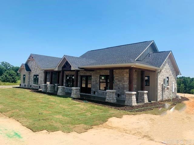 view of front of home with board and batten siding, a shingled roof, stone siding, and a front lawn