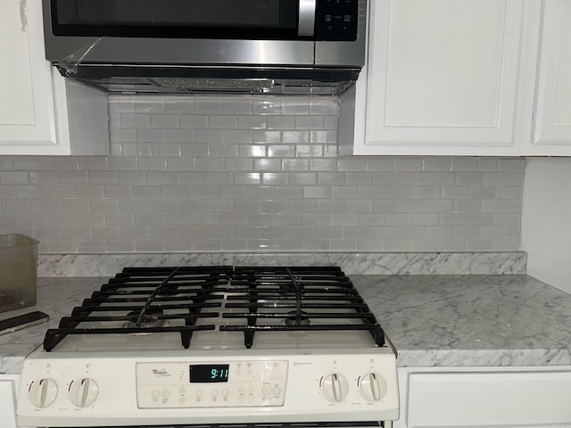 kitchen view of gas range, stainless steel microwave, white cabinetry, and backsplash
