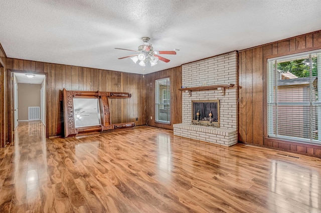 4204 Fox Hill Rd, North Little Rock, AR 72116 - unfurnished living room with a textured ceiling, wood walls, wood finished floors, a ceiling fan, and a fireplace