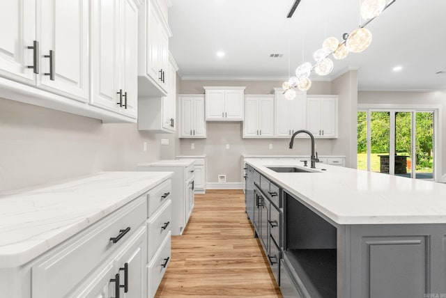 kitchen featuring a sink, light wood finished floors, an island with sink, white cabinets, and gray cabinetry