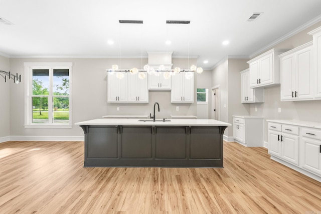 kitchen with a sink, light wood finished floors, an island with sink, baseboards, and white cabinetry