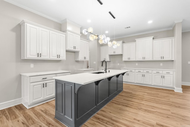 kitchen featuring light wood-type flooring, a center island with sink, white cabinetry, crown molding, and baseboards