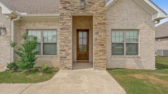 107 Hidden Creek Dr, Brookland, AR 72417 - view of exterior entry featuring central air condition unit, a lawn, brick siding, and a shingled roof