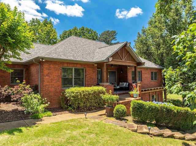 view of front of house with a shingled roof, brick siding, and a front yard