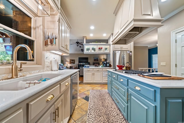 kitchen with appliances with stainless steel finishes, a sink, stone tile floors, light countertops, and crown molding