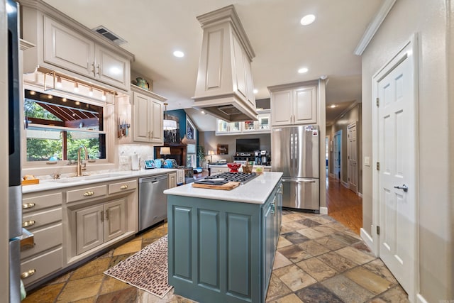 kitchen with appliances with stainless steel finishes, stone tile floors, a sink, light countertops, and a kitchen island
