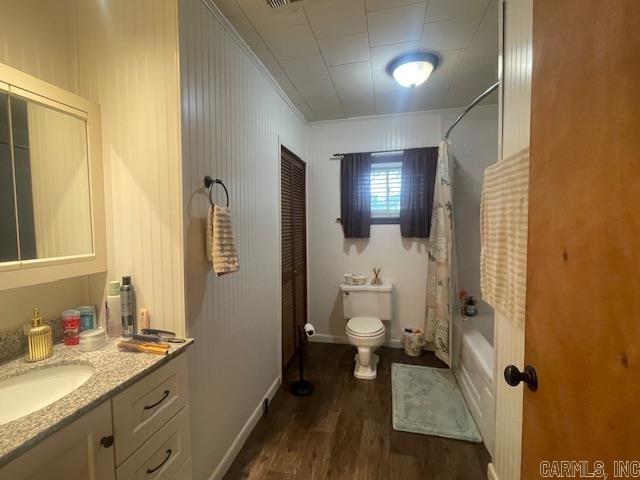 bathroom with wood finished floors, vanity, toilet, shower / tub combo with curtain, and baseboards