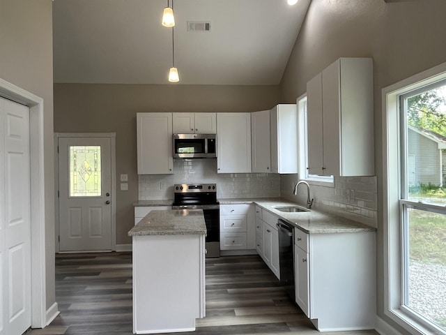 kitchen with appliances with stainless steel finishes, a sink, vaulted ceiling, a center island, and backsplash