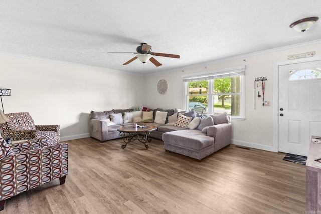 living area featuring light wood-type flooring, baseboards, a ceiling fan, and ornamental molding