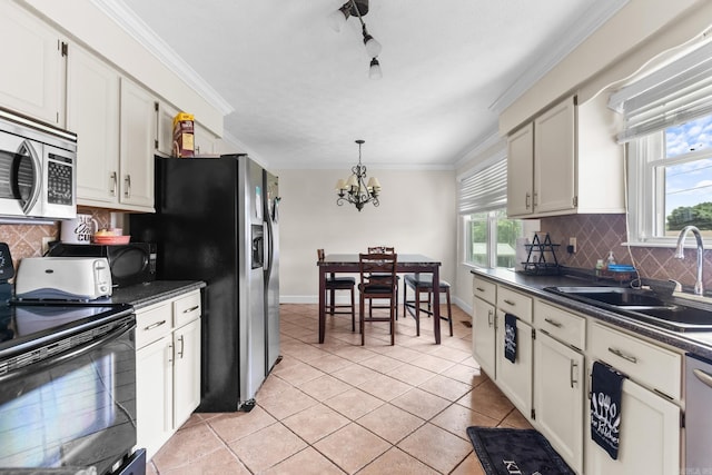 kitchen with appliances with stainless steel finishes, dark countertops, a chandelier, a sink, and plenty of natural light