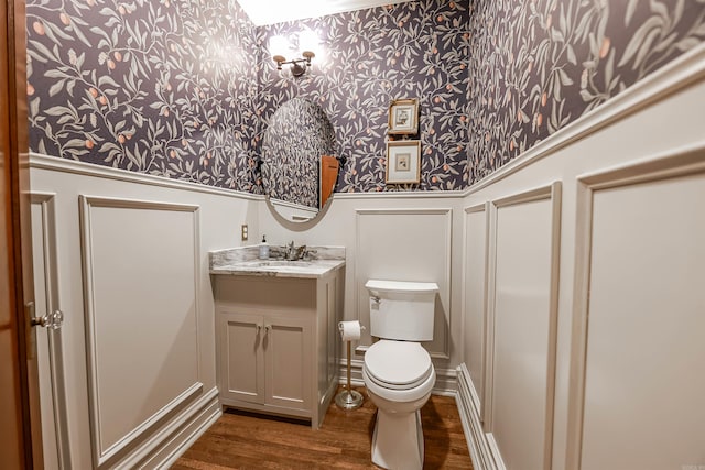 837 Maple St, Camden, AR 71701 - half bath with wallpapered walls, a decorative wall, vanity, wood finished floors, and toilet