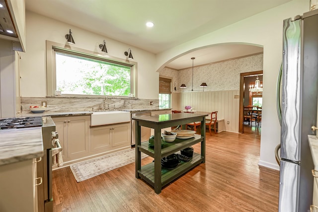 837 Maple St, Camden, AR 71701 - kitchen featuring stainless steel appliances, a sink, arched walkways, wainscoting, and light wood-style flooring