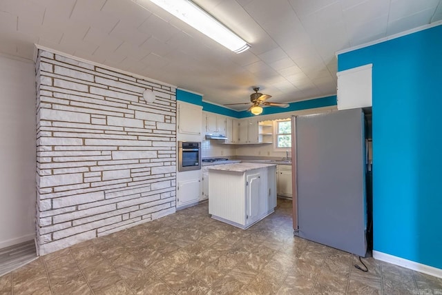 kitchen with appliances with stainless steel finishes, under cabinet range hood, a ceiling fan, a kitchen island, and tile patterned floors