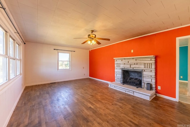 unfurnished living room featuring ceiling fan, wood finished floors, a stone fireplace, crown molding, and baseboards