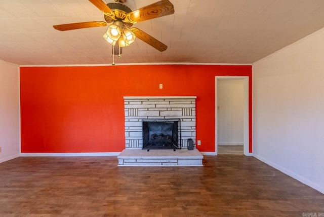 unfurnished living room featuring ornamental molding, wood finished floors, ceiling fan, a stone fireplace, and baseboards