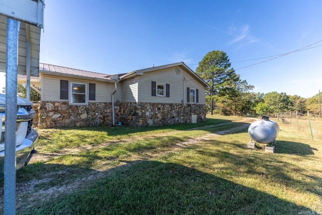view of side of home featuring stone siding, a yard, and metal roof