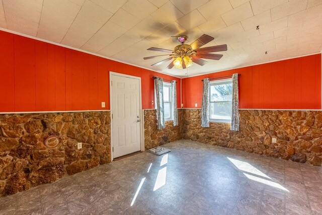 unfurnished room featuring a ceiling fan, wainscoting, tile patterned floors, ornamental molding, and wooden walls
