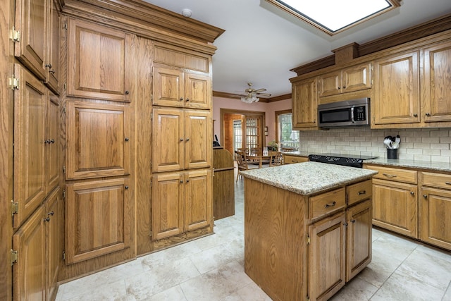16 Masters Place Dr, Maumelle, AR 72113 - kitchen featuring stainless steel microwave, decorative backsplash, a kitchen island, ornamental molding, and brown cabinets