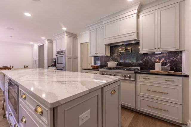 40 Tennyson Ct, North Little Rock, AR 72116 - kitchen featuring appliances with stainless steel finishes, a center island, decorative backsplash, light stone countertops, and wood finished floors