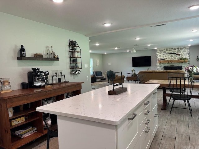 9 Whispering Dr, Alexander, AR 72002 - kitchen with white cabinets, light stone counters, light wood finished floors, a stone fireplace, and a center island