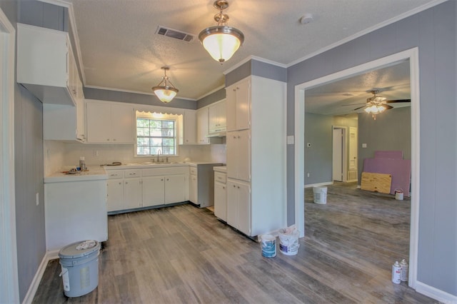 1320 Abigail St, Little Rock, AR 72204 - kitchen with a sink, a textured ceiling, wood finished floors, crown molding, and white cabinetry