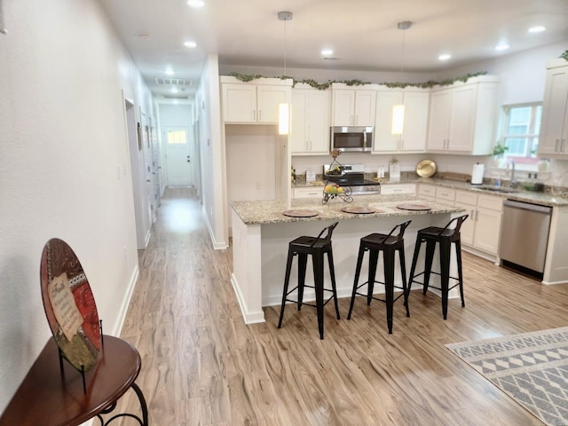 1418 S Martin St, Little Rock, AR 72204 - kitchen featuring appliances with stainless steel finishes, a sink, white cabinets, a center island, and light wood-style floors
