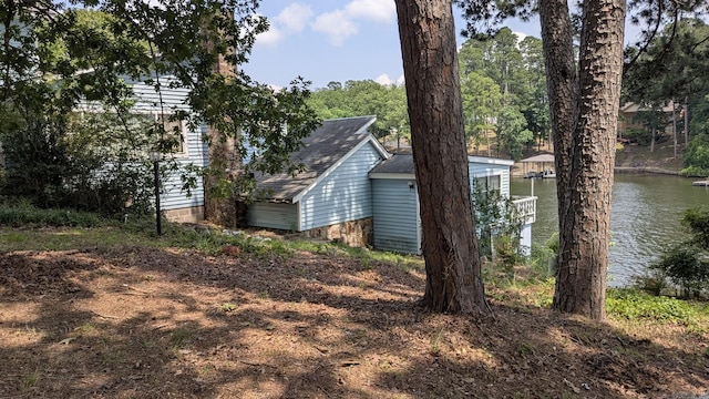 view of property exterior featuring a water view, a boat dock, and a shingled roof