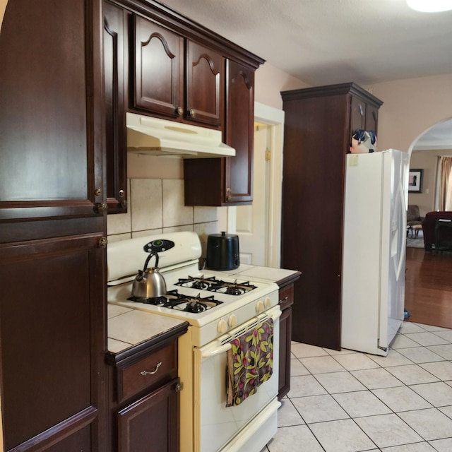 1401 S Schiller, Little Rock, AR 72202 - kitchen featuring white appliances, under cabinet range hood, arched walkways, dark brown cabinetry, and light tile patterned floors