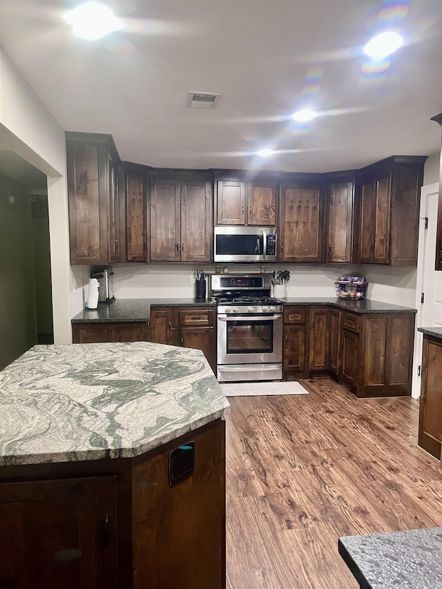 88 Cobblestone Rd, Plumerville, AR 72127 - kitchen with appliances with stainless steel finishes, dark wood-type flooring, dark brown cabinets, stone countertops, and a kitchen island