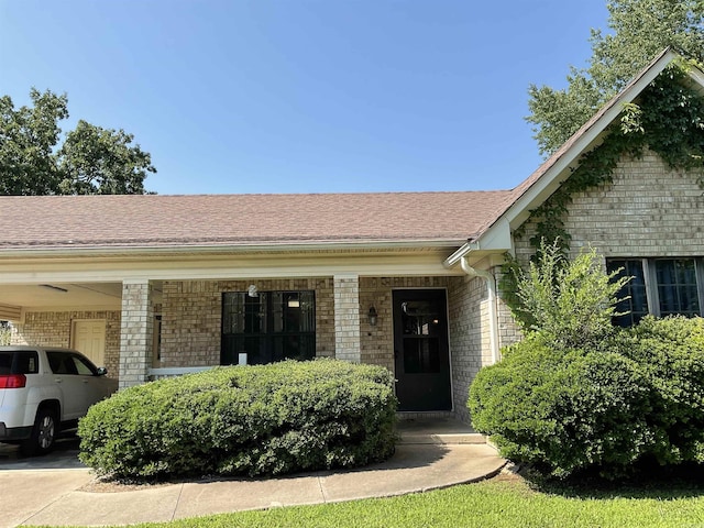 view of front of property featuring brick siding, a shingled roof, and a carport