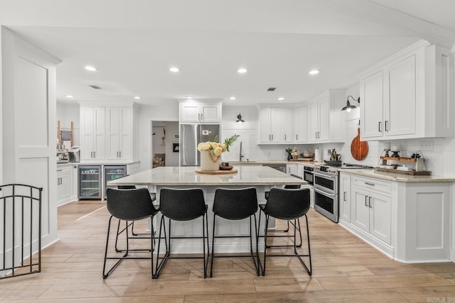 14320 Bradley Rd, Maumelle, AR 72113 - kitchen featuring wine cooler, appliances with stainless steel finishes, decorative backsplash, white cabinets, and a breakfast bar area