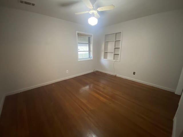 spare room featuring dark wood finished floors, baseboards, built in shelves, and a ceiling fan