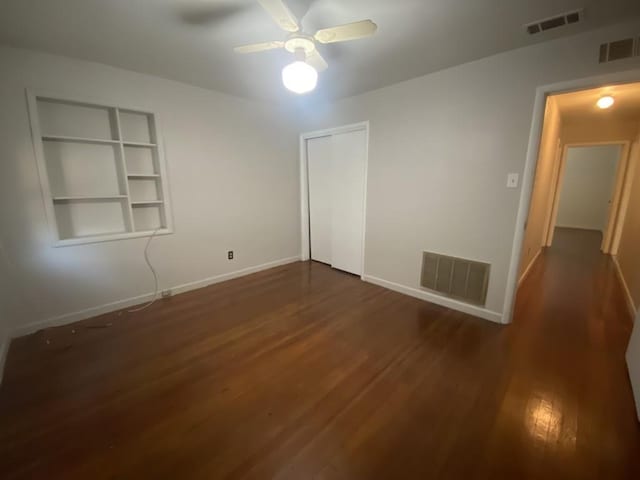 empty room with wood finished floors, baseboards, ceiling fan, and built in shelves