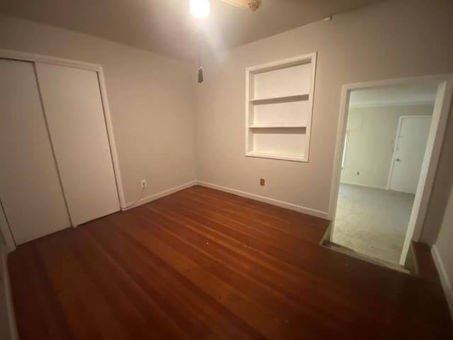 unfurnished bedroom featuring wood finished floors, baseboards, and a closet