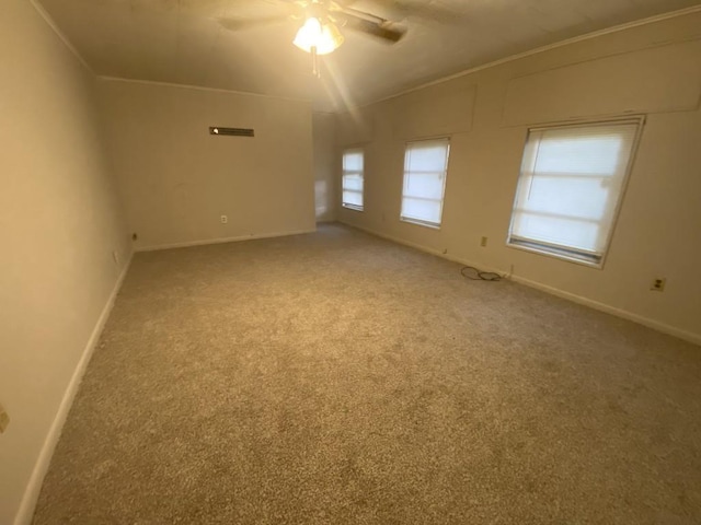 carpeted empty room with a ceiling fan, baseboards, and crown molding